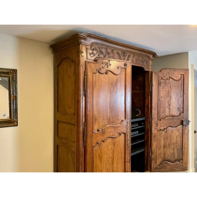 An imposing 1814 French Provincial style walnut armoire capped with a deeply carved crown moulding and a huge pair of a...