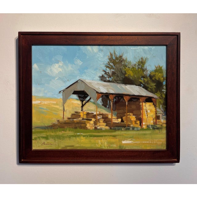 This oil painting depicts a rustic shed with a metal roof, surrounded by stacks of hay bales that convey a sense of...