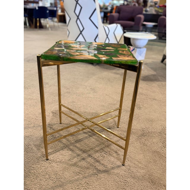 This striking accent table features a vibrant green resin top embedded with natural stone fragments, creating a unique...