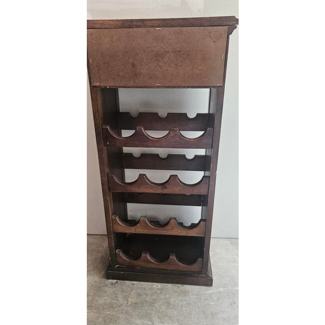 This BUTLER vintage dark wood wine rack cabinet features a top pull-out drawer with a brushed brass-finish front panel and...