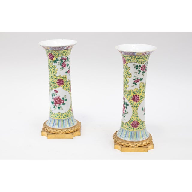 Small gu-form porcelain vases decorated with pink family enamels on a yellow background, adorned with green interlace....