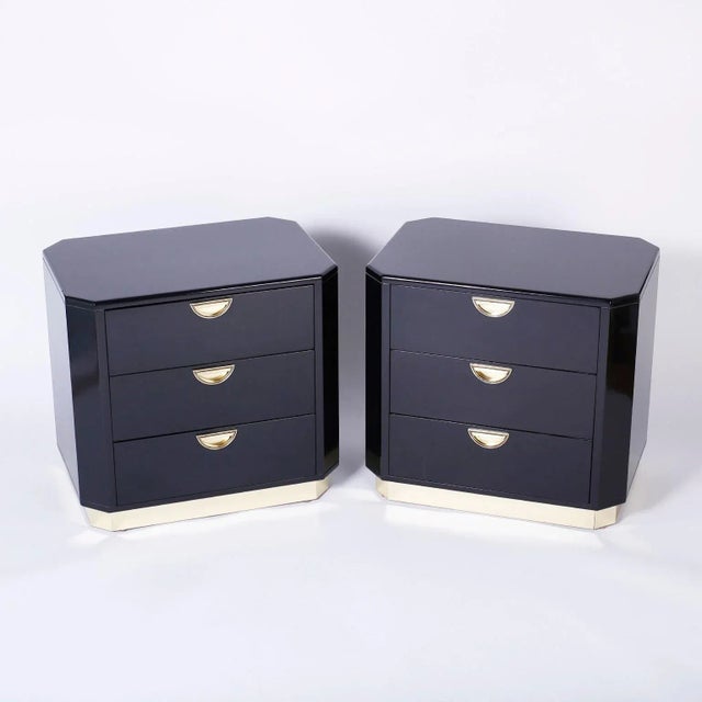 In voque pair of three drawer black lacquered nightstands with a sleek refined form, inset brass pulls and a brass block...