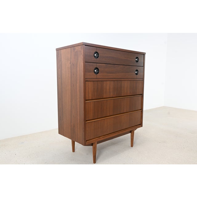 Crafted by Stanley Furniture, this striking mid-century modern highboy dresser showcases beautifully grained walnut and a...