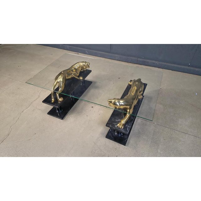Stunning coffee table with two brass jaguar sculptures mounted on marble column bases and a clear rectangular glass top....