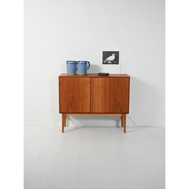 1950s teak bar cabinet with two folding doors and a mirrored interior with bottle holder. Elegant 1950s Scandinavian teak...