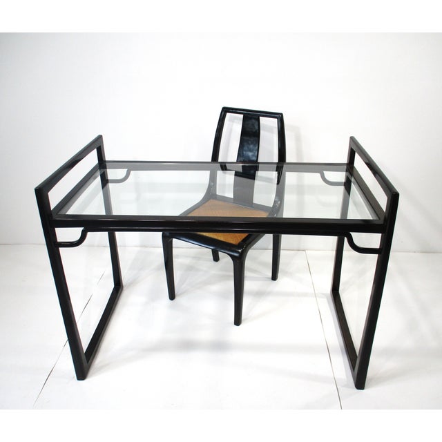 A very well-crafted ebony toned sculptural wooden desk with glass top and matching chair with the seat in a tight woven...