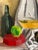 This expressive still life painting features a carefully arranged composition of bottles, fruit, and softly draped fabric,...