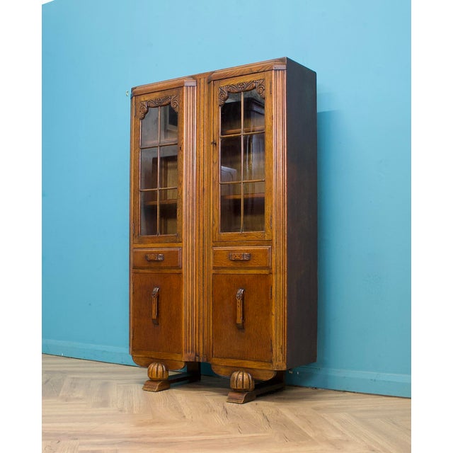 A well-made 1930s oak display cabinet with classic Art Deco styling. Featuring glazed doors with carved detailing, fluted...