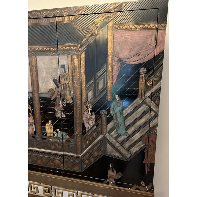 Fine black cabinet with detailed painted chinoiserie scenery. Cabinet sits on brass stand with greek key design. Cabinet...
