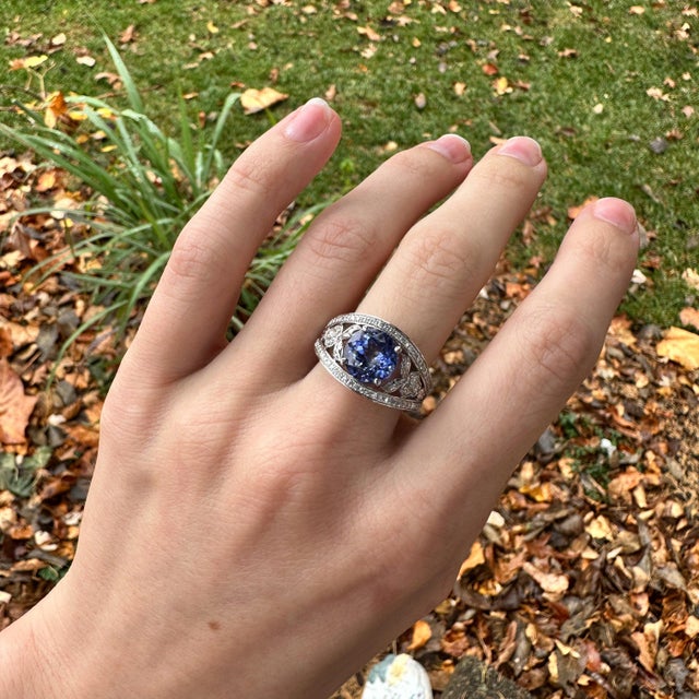 A tanzanite rests in a deep violet-blue at the heart of this solid 14K white gold ring, flanked by seventy earth-mined...