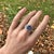 A tanzanite rests in a deep violet-blue at the heart of this solid 14K white gold ring, flanked by seventy earth-mined...