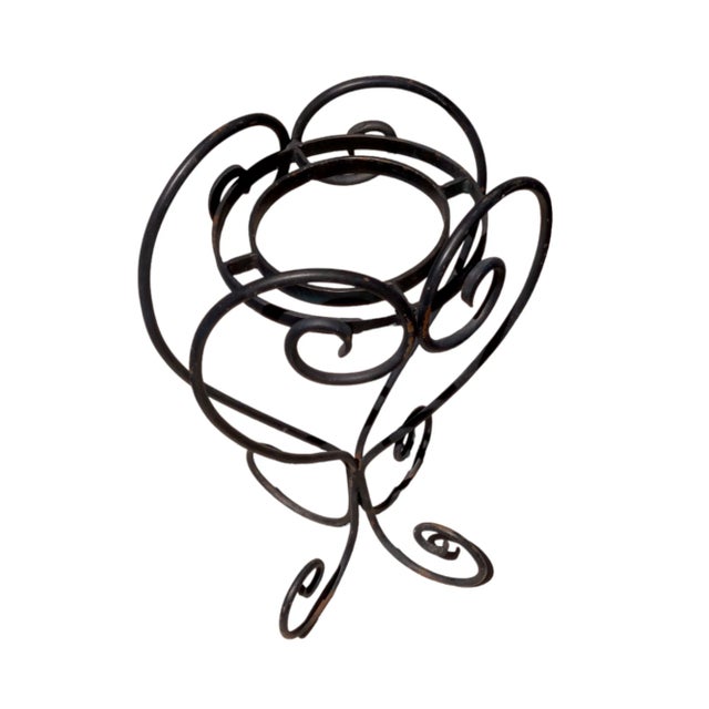 A black scrolling wrought iron plant stand designed to accommodate a single potted plant . the garden item has both...