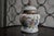 A charming vintage porcelain ginger jar featuring hand-painted figural and landscape scenes in the chinoiserie style....