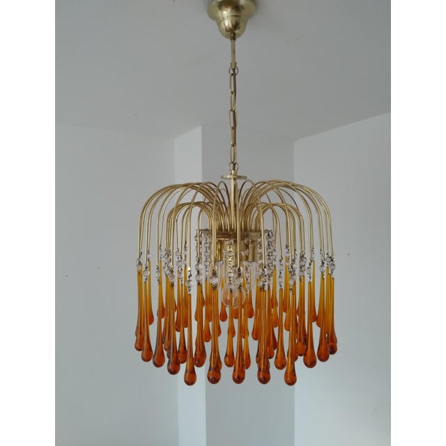 Elegant 1970s Murano glass chandelier attributed to Paolo Venini. The brass structure features cascading amber teardrop...