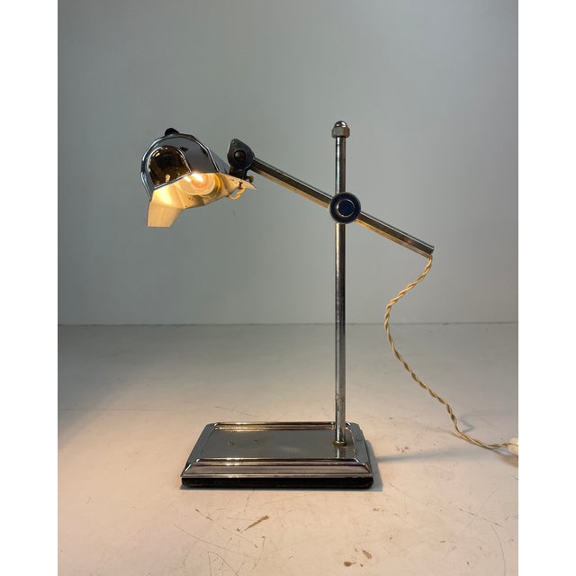 Elegant art deco desk lamp crafted in chrome-plated metal; it features a weighted rectangular base, a fixed vertical...