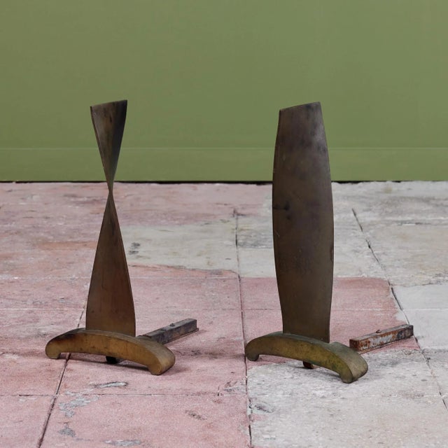Pair of bronze modernist andirons. The andirons feature a ribbon like twisted front with curved footed detail. A beautiful...