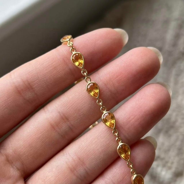 This elegant bracelet features a continuous array of luminous, teardrop-shaped stones seamlessly linked by a delicate...