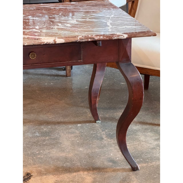 A French mahogany table fitted with a rectangular marble top resting above a single drawer set into the apron. The drawer...