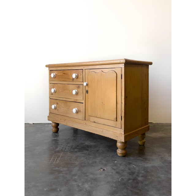 This antique 19th century English pine sideboard features three drawers on the left and a spacious cabinet on the right, a...