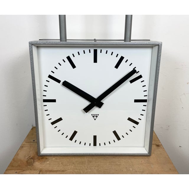 This square double-sided railway, school or factory clock was produced by Pragotron, in former Czechoslovakia, during the...