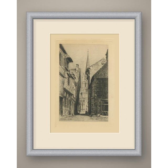 A narrow cobbled street in an old Norman town leads the eye straight to a church tower at its far end. On the left rise...