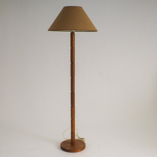 A vintage floor lamp with a beautifully turned, segmented wooden stem that highlights the natural grain of the wood,...