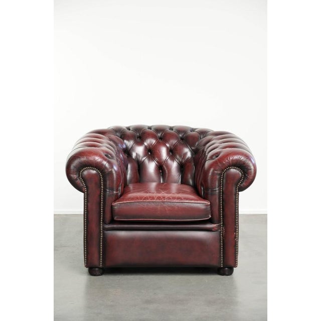 This distinctive English Chesterfield club armchair is made of cowhide leather in a timeless red color. The armchair has a...