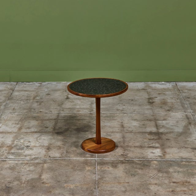 Round side table by Gordon & Jane Martz. The table top is inlaid with black ceramic coin tiles. The frame, base and...