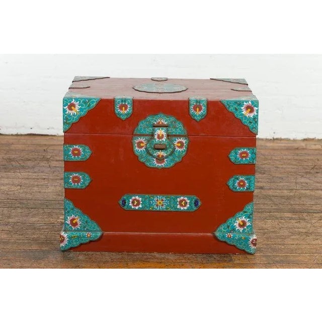 A vintage Chinese blanket chest from the mid 20th century with red lacquer ground, cloisonné décor and lateral handles....
