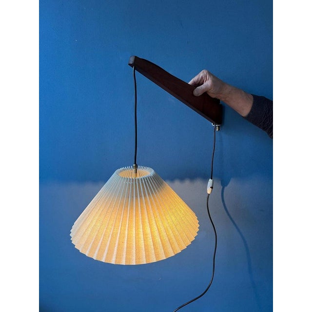 Teak wood 'rod' wall lamp with off-white pleated fabric shade. The position of the teak wood rod can easily be adjusted,...