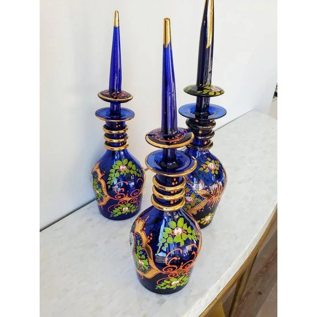 A scarce set of three fine quality Bohemian enameled cobalt art glass decanters, exquisitely made for the Persian market,...