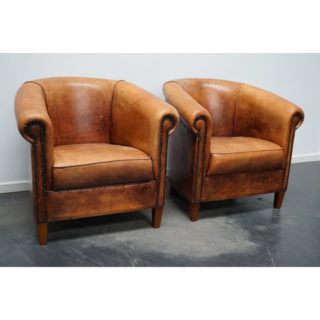 This pair of cognac-colored leather club chairs come from the Netherlands. They are upholstered with cognac-colored...