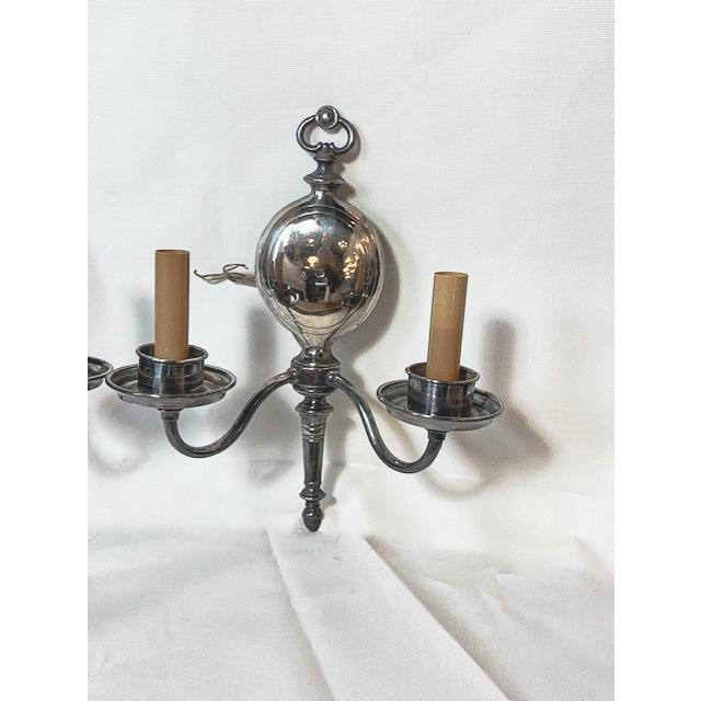 This refined pair of double-arm sconces features a sophisticated silver finish and intricately detailed wall mounts that...