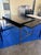 Elegant black writing desk featuring a sleek, expansive work surface paired with a slender brass-finish metal base. The...