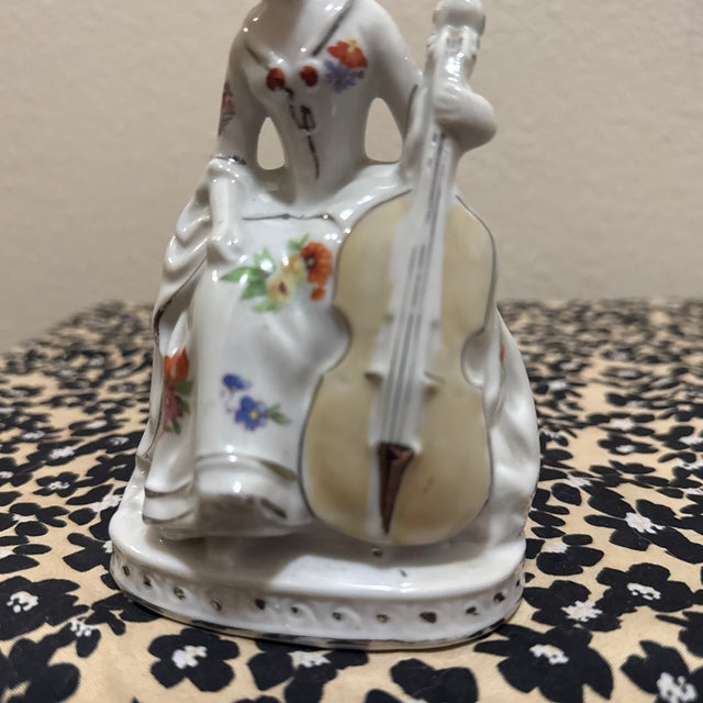A charming vintage porcelain figurine depicting a Victorian-era lady seated while gracefully playing a cello.