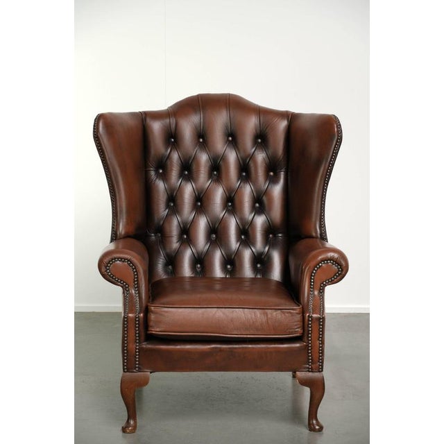 This beautiful brown English-style Chesterfield wingback chair is made of cowhide leather and offers a comfortable seat....