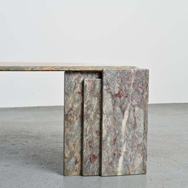 Coffee table composed of a thick marble top with multicolored veins, blending shades of blue, ochre, and deep red. The...