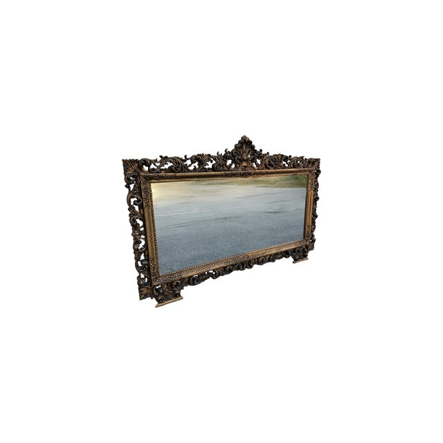 This imposing baroque mirror features a rich gilded wood frame, decorated with elaborate carvings of curlicues and floral...