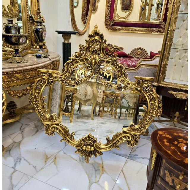 Stunning vintage French Baroque wall mirror featuring an exceptionally ornate frame adorned with elaborate botanical...