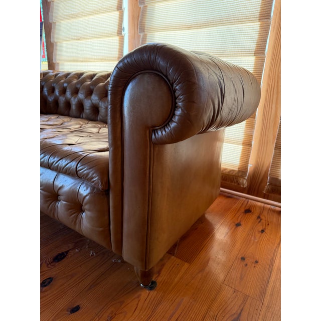A timeless leather Chesterfield sofa featuring deep button tufting, rolled arms, and a low, grounded profile. Upholstered...