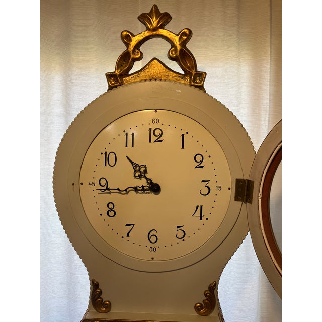 Elegant Swedish Mora longcase clock featuring a distinctive sculptural silhouette, cream-painted case, and decorative gilt...