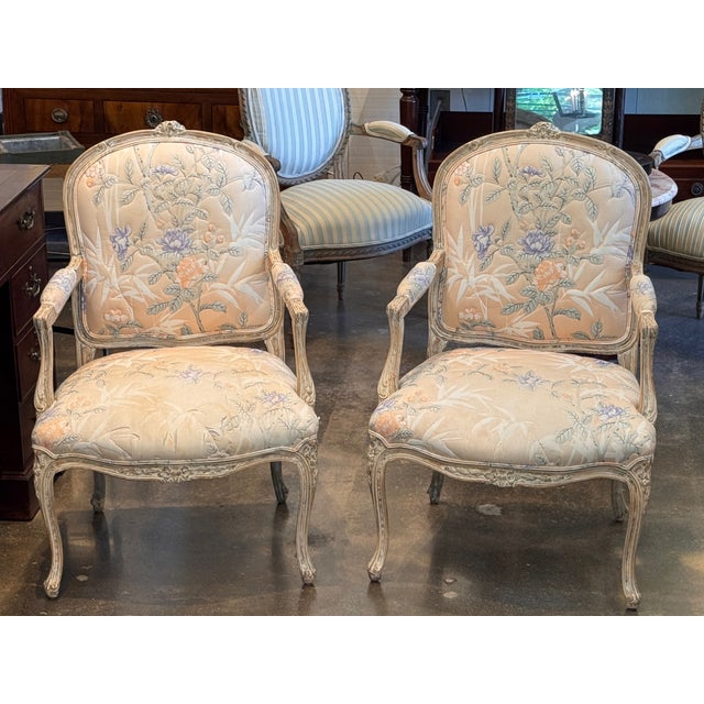A well-made pair of Louis XV style open armchairs with painted frames in a warm cream finish. The carved frames have the...