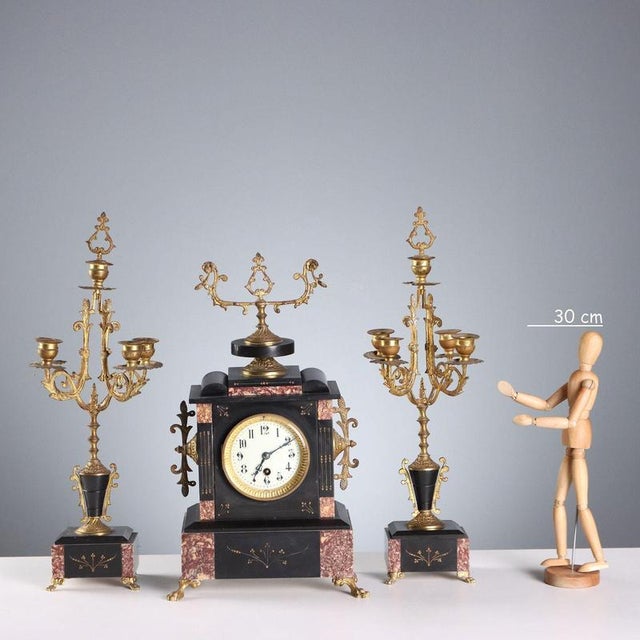 Fireplace triptych in black marble, breccia, and gilded bronze. The clock rests on feline paw feet. The enameled metal...