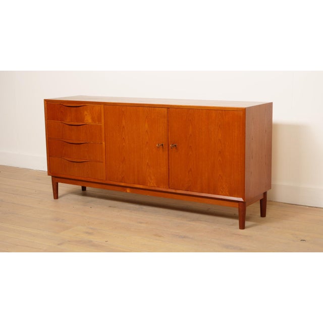 This elegant vintage teak sideboard brings a stylish and cosy atmosphere to any room. The sleek design and warm wood tone...