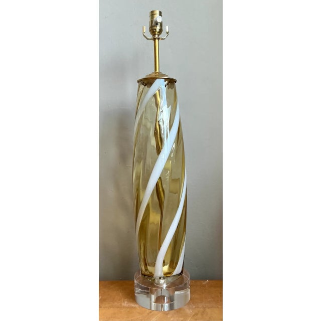 This vintage Murano table lamp features a hand-blown glass body where warm amber and white hues spiral gracefully around...