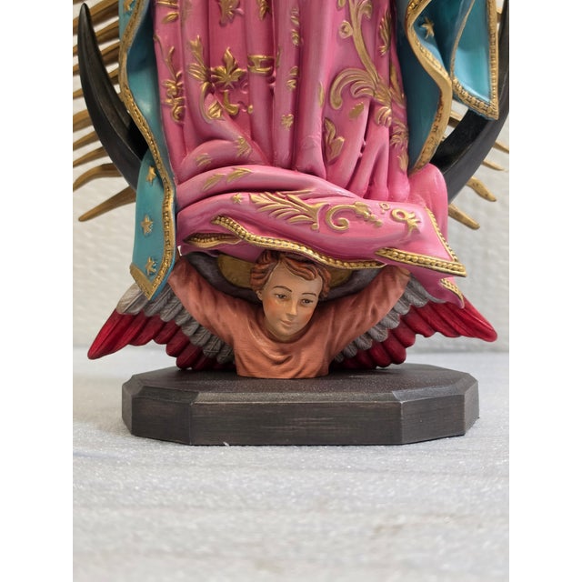 Our Lady of Guadalupe is depicted with hands joined in prayer, a star-decorated green mantle and a rose-colored gown,...