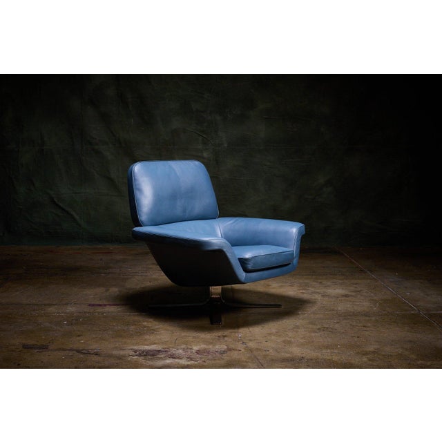 Minotti Blake pair of swivel lounge armchairs upholstered in blue leather with wide angular arms and four-star metal...
