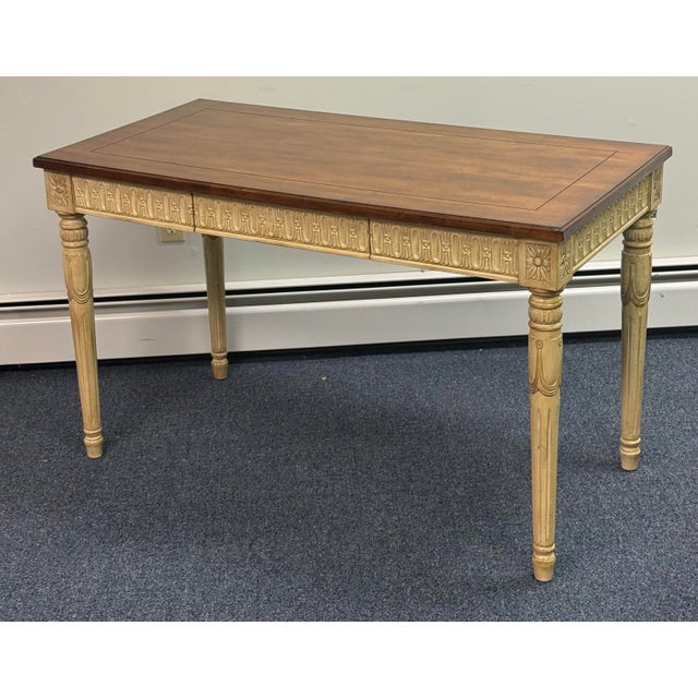 Elegant Neoclassical-style writing table featuring a warm wood top with a finely outlined inset border, beautifully...