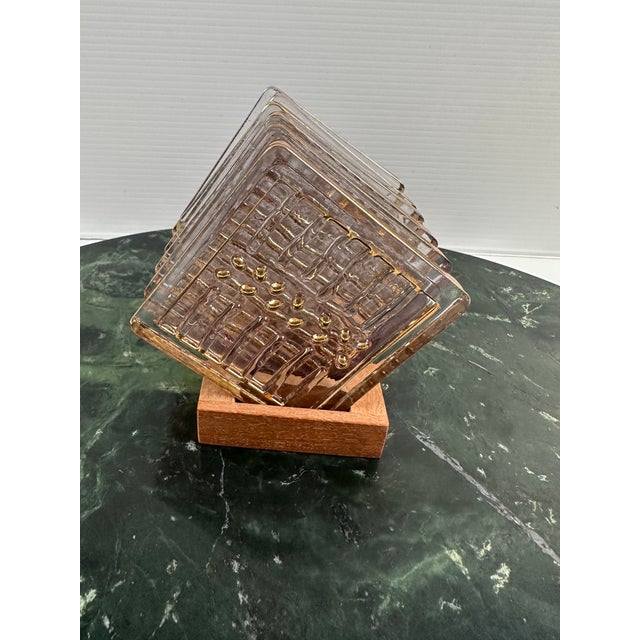 A refined vintage coaster set by Stephen Smyers, featuring six square clear art glass coasters with applied gold...