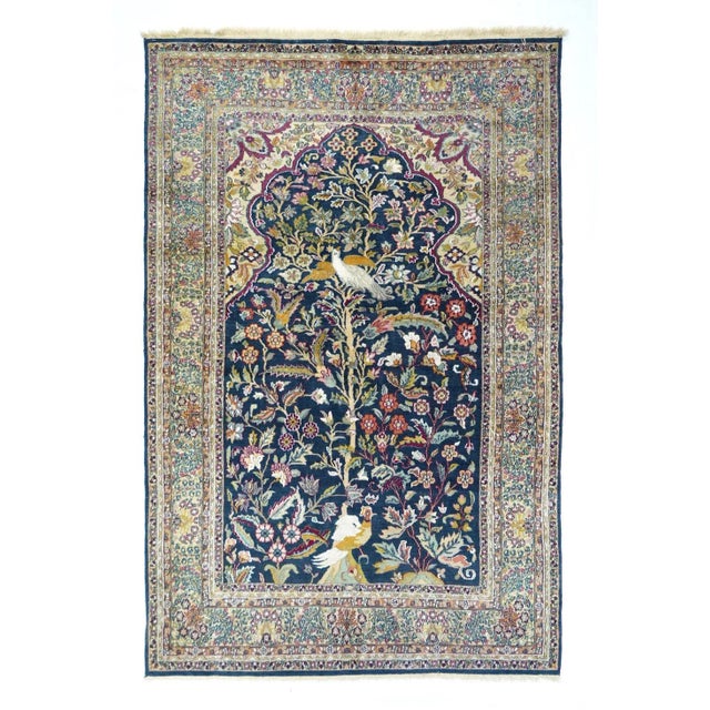 The scalloped-arch dark blue field shows a central tall "tree of life" with an elaborate bird perching at the base and a...